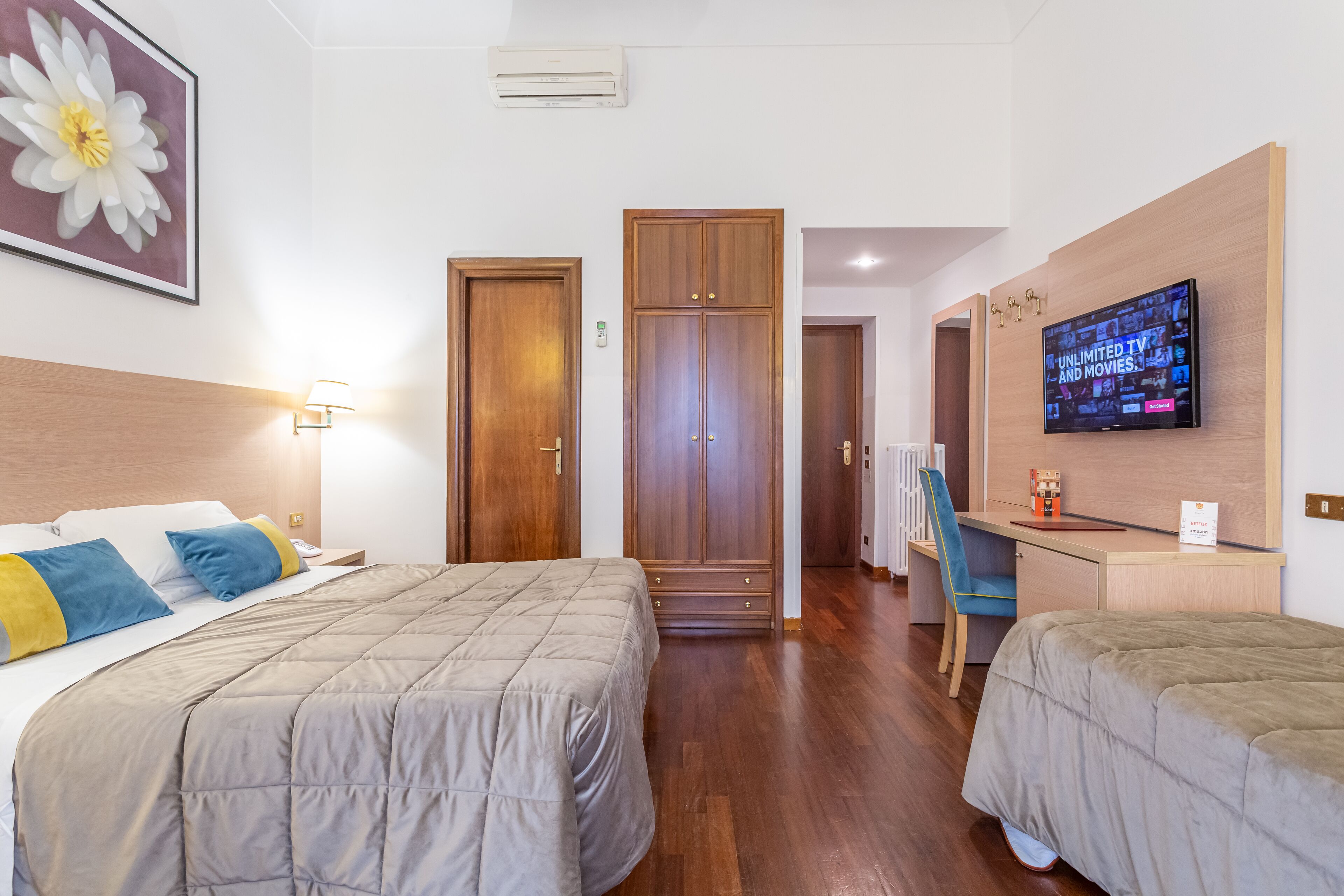 Ein Hotelzimmer mit zwei Betten, einem Schreibtisch mit Fernseher und einem Kleiderschrank.