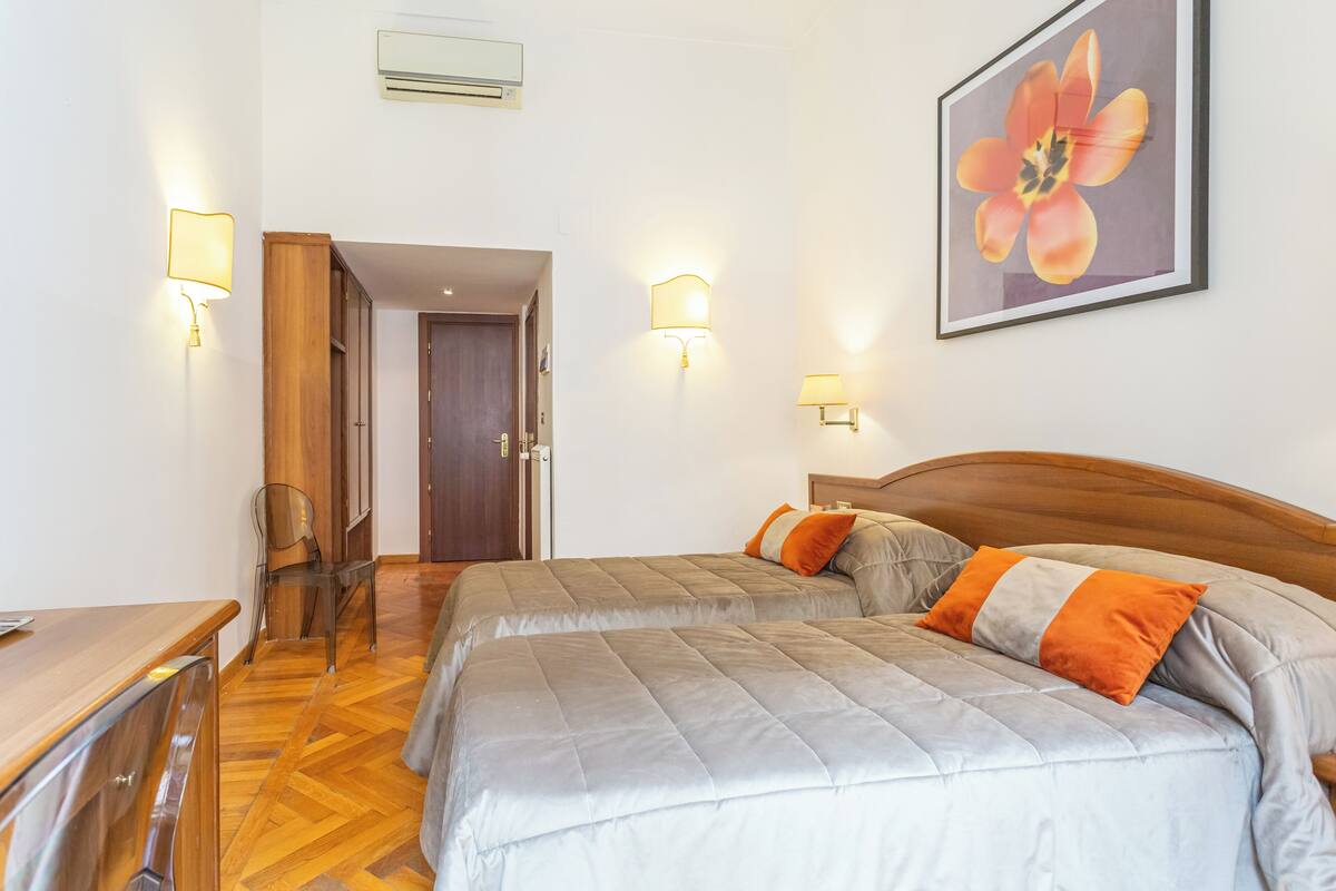 A hotel room with two beds, a wooden headboard, a desk, and a chair.