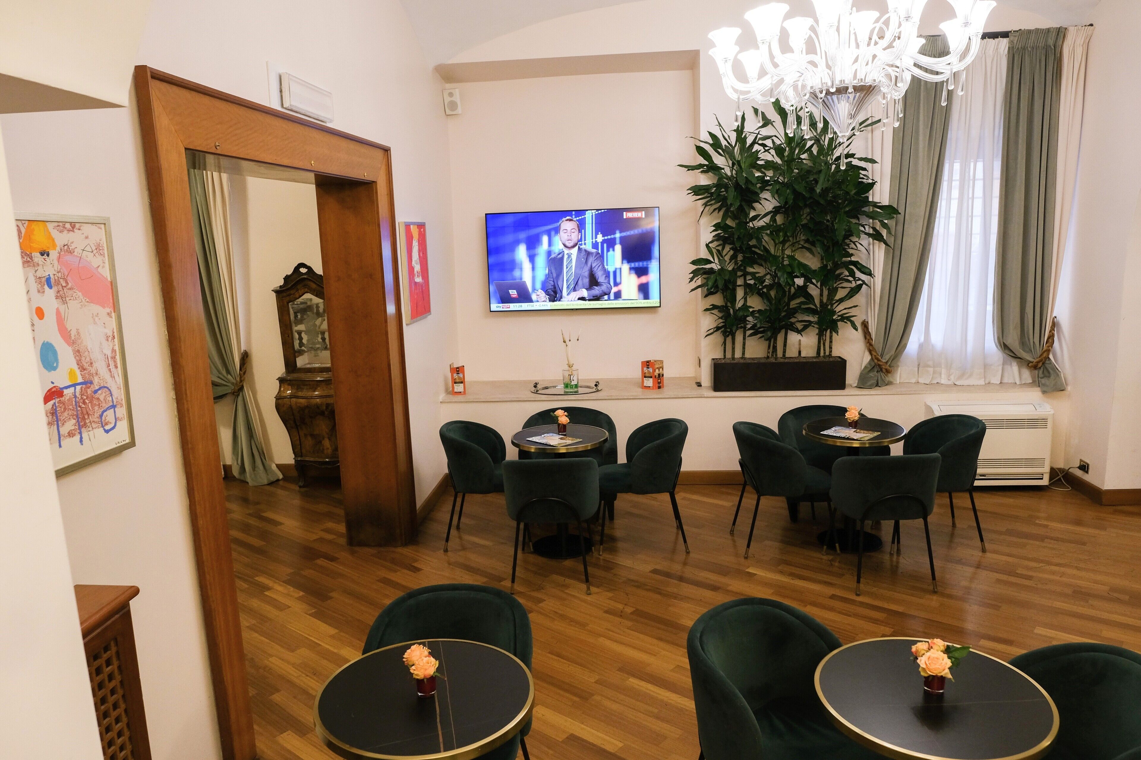 A hotel room with a television, green chairs, a wooden floor, and a large plant.
