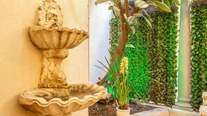 Una fuente de piedra con una figura decorativa, una planta en maceta y una pared cubierta de follaje verde.