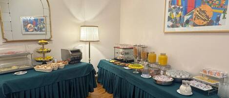 A buffet setup with various food items and beverages, a grill, and a framed artwork on the wall.