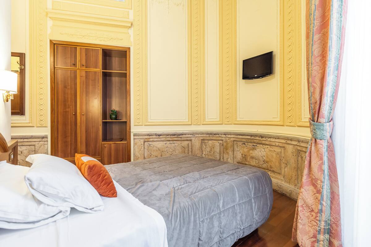 A hotel room with a bed, a wardrobe, a television, and a decorative curtain.