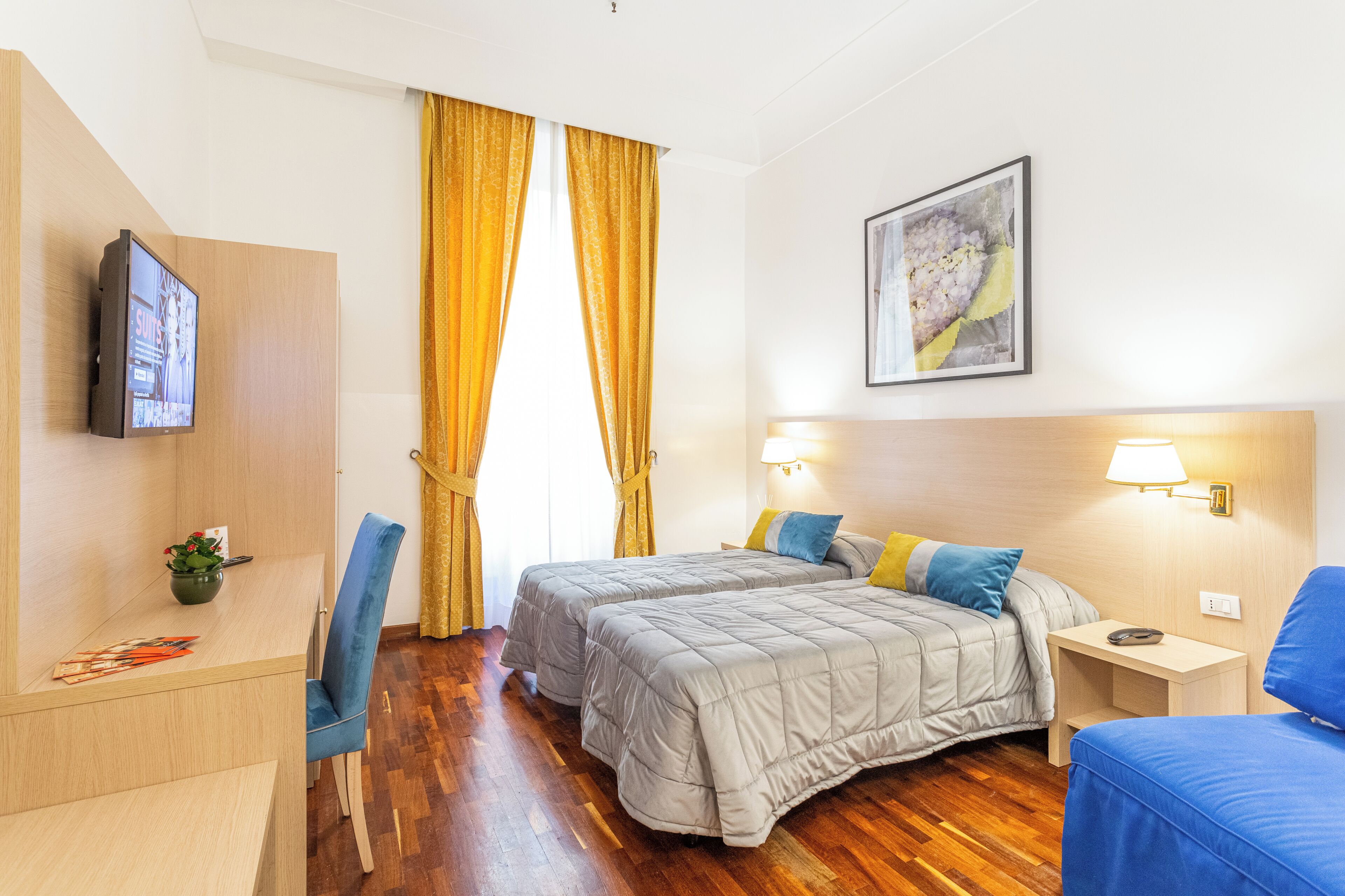 A hotel room with two beds, a desk, a chair, a TV, and a painting on the wall.