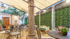 Un café con piso a cuadros, sillas de metal, una columna de piedra y una pared cubierta de hiedra verde.
