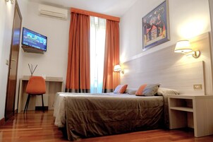 Habitación de hotel con cama, escritorio, silla, televisor y un cuadro en la pared.