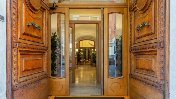 Una entrada imponente con puertas de madera ornamentadas y un piso negro con un logotipo de escudo.