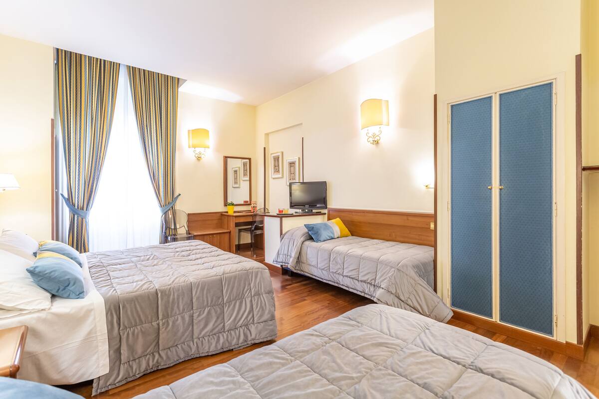 A hotel room with three beds, a desk with a computer, a TV, and a wardrobe.