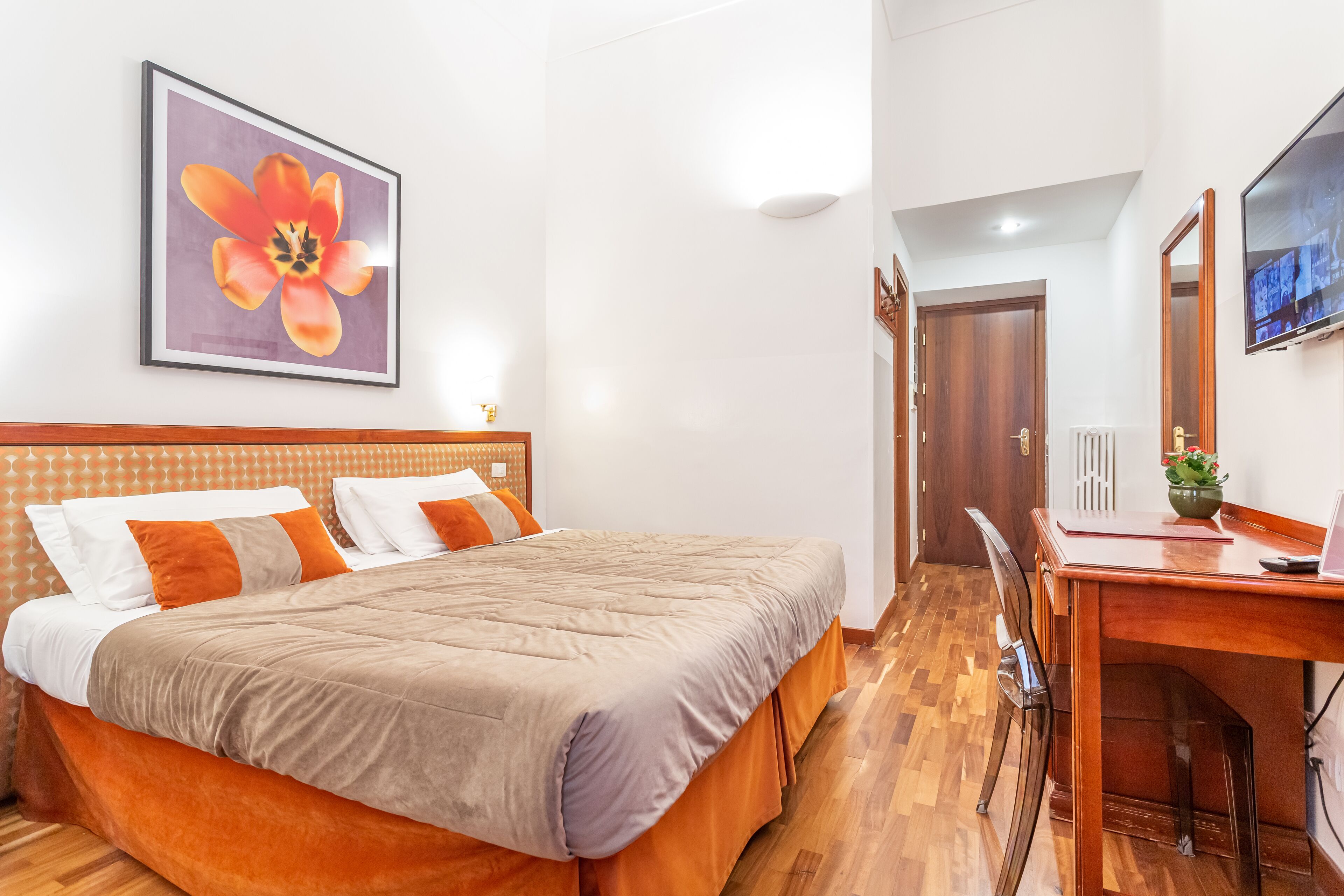 Habitación de hotel con cama, escritorio, silla, televisión e imagen enmarcada en la pared.