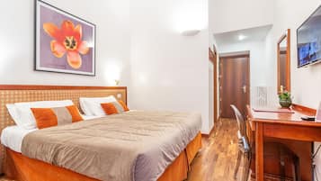 Habitación de hotel con cama, escritorio, silla, televisión e imagen enmarcada en la pared.