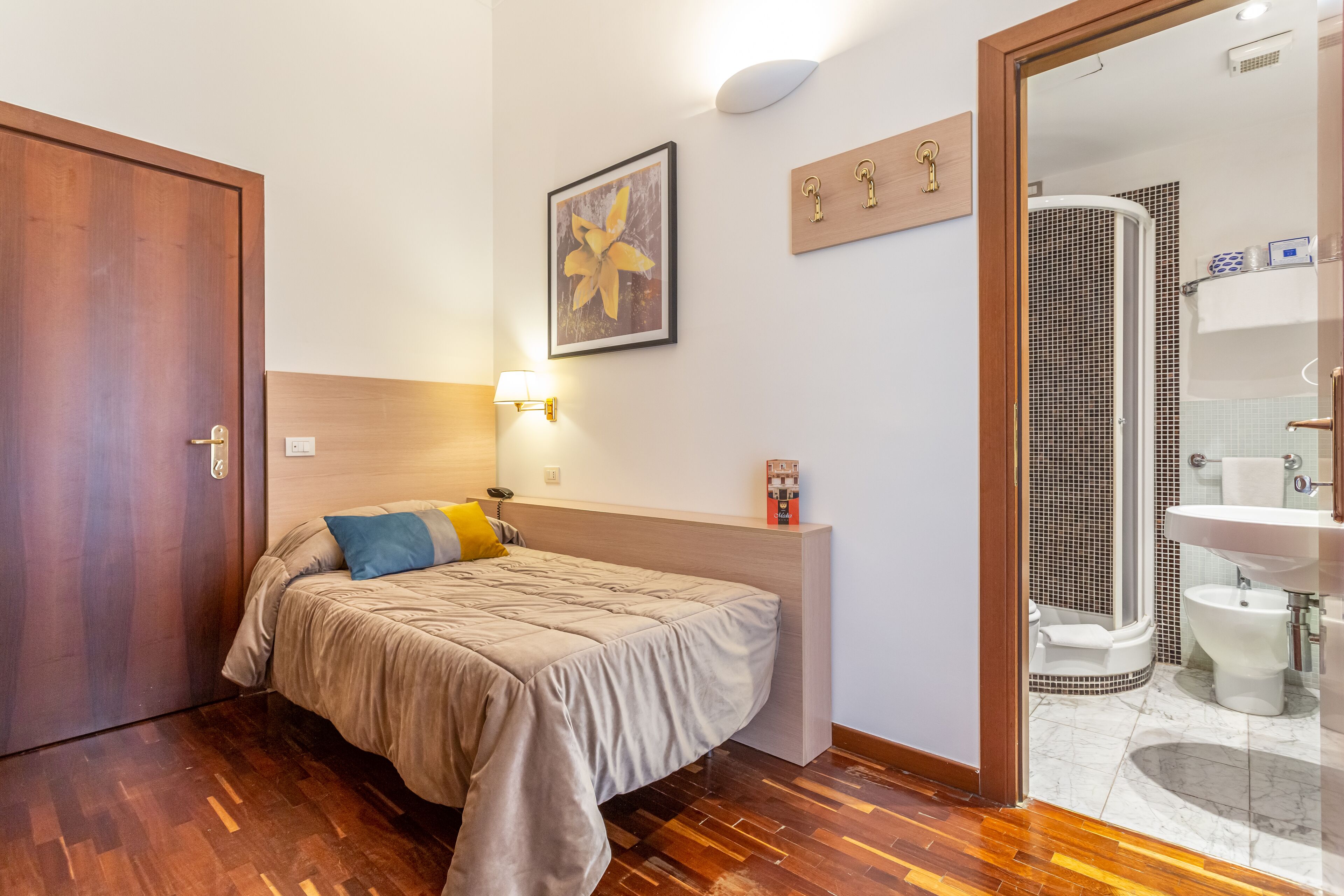 Hotelkamer met een bed, een bedlampje, een inlijsting foto aan de muur, een houten plankje met sleutels, en een badkamer zichtbaar door een geopende deur.