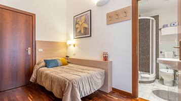 Hotelkamer met een bed, een bedlampje, een inlijsting foto aan de muur, een houten plankje met sleutels, en een badkamer zichtbaar door een geopende deur.