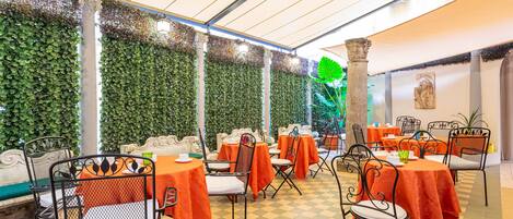 An indoor dining area with tables covered in orange tablecloths, metal chairs, and a checkered floor.