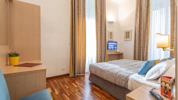 Une chambre d’hôtel équipée d’un lit, d’une table de chevet, d’une télévision, d’une lampe et d’un petit bureau agrémenté d’une plante.