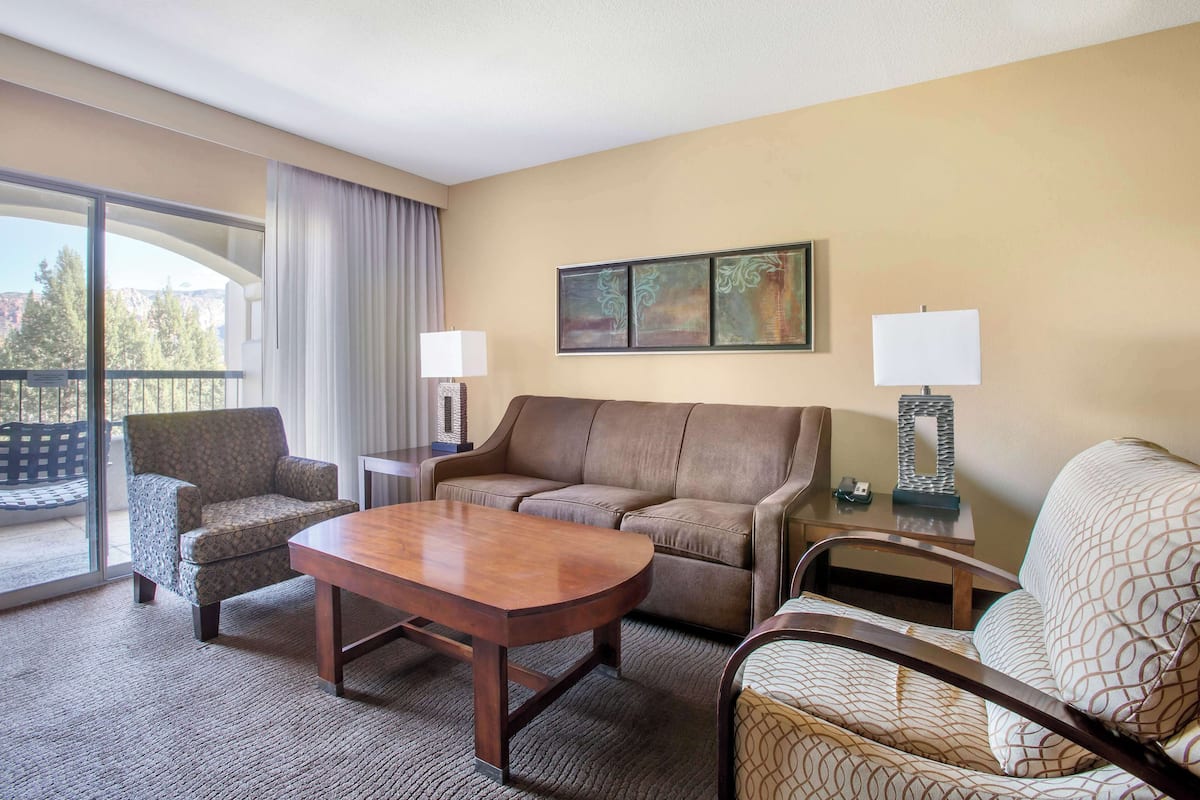 A hotel room with a large window, a sofa, a chair, a table, and two lamps.