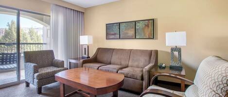 Habitación de hotel con un ventanal grande, un sofá, una silla, una mesa y dos lámparas.
