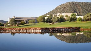 A large building with multiple sections, a pond reflecting the structure, and a hilly landscape in the background.