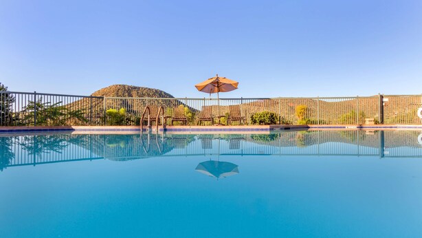A swimming pool with a metal fence, a sun umbrella, and a mountain in the background.