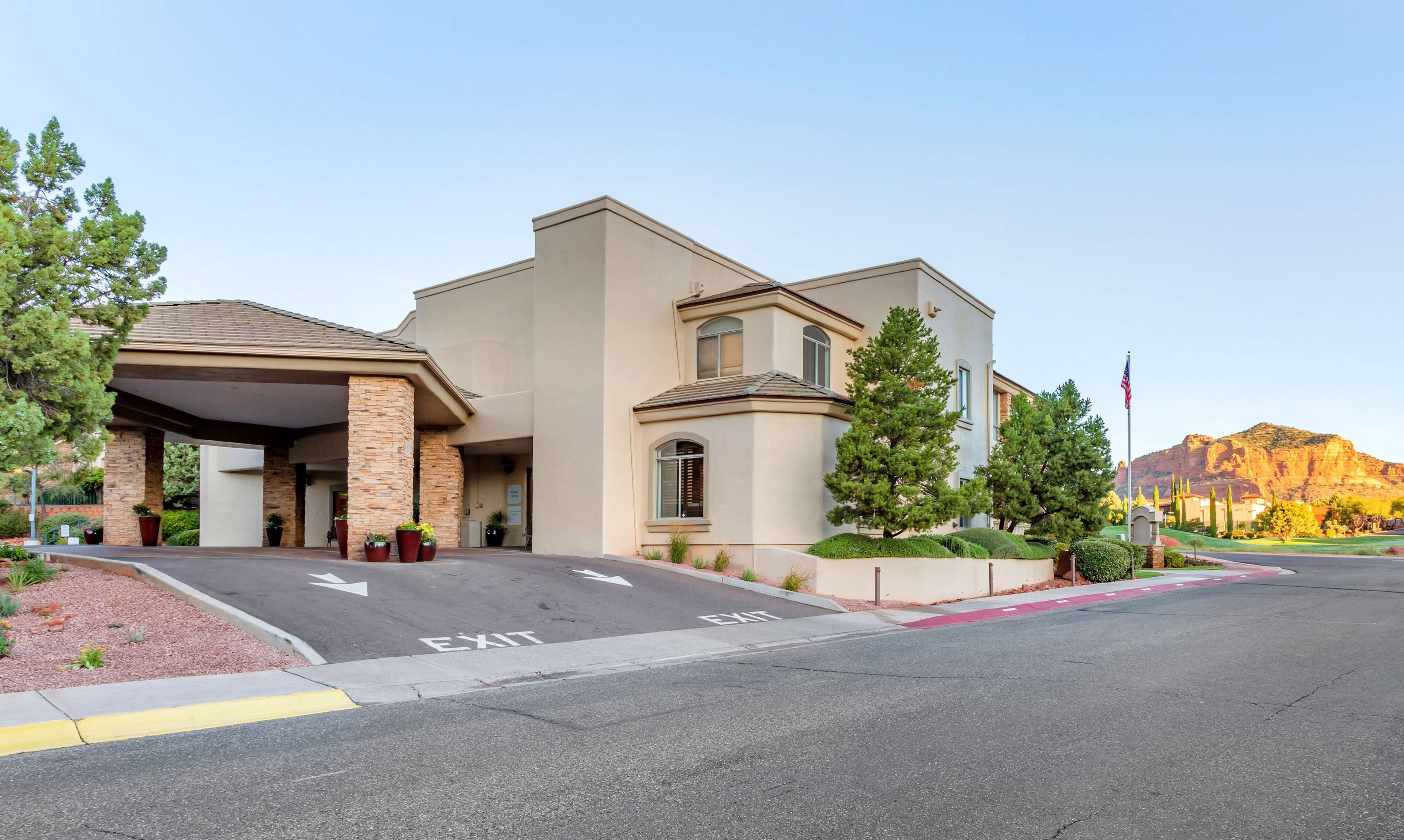 A modern hotel with a covered entrance, a landscaped driveway, and a mountain backdrop.