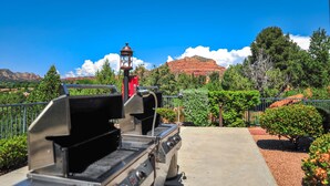A barbecue grill with a view of red rock formations and greenery in the background.