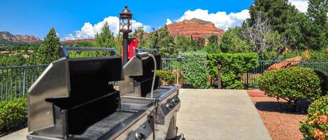 A barbecue grill with a view of red rock formations and greenery in the background.