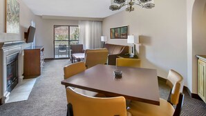 A hotel room with a dining area, a fireplace, a balcony with a view, and a chandelier.
