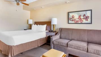 A hotel room with two beds, a sofa, a ceiling fan, a nightstand, lamps, and a framed artwork on the wall.