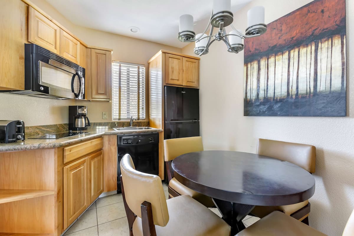 A kitchen with wooden cabinets, a microwave, a refrigerator, and a dining table with chairs.
