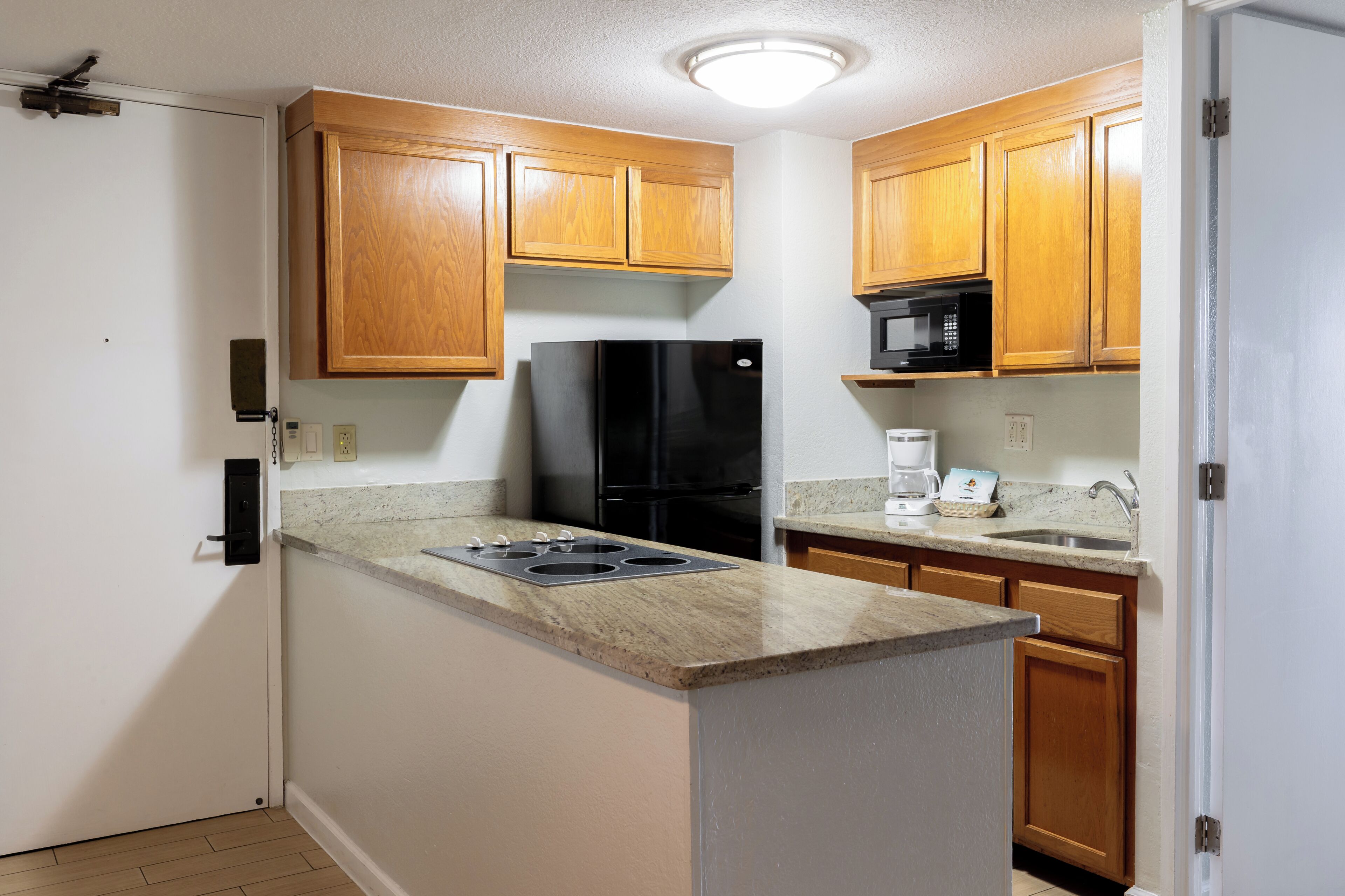 A compact kitchen with wooden cabinets, a black refrigerator, a microwave, and a coffee maker.