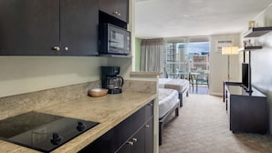 A kitchenette with a microwave, coffee maker, and a small dining area with a table and chairs. - Skyline Island Colony Hotel (Honolulu)