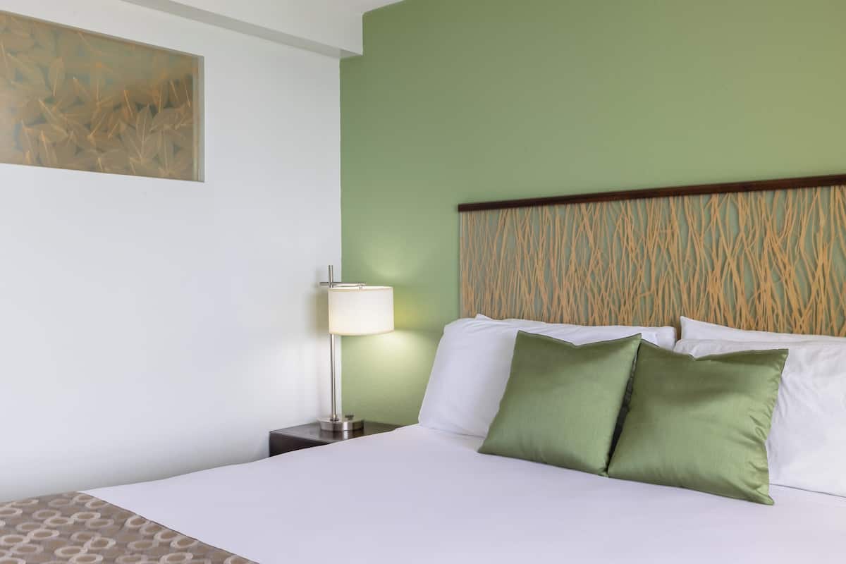 A hotel room with a bed, a nightstand, a lamp, and a wall art piece.