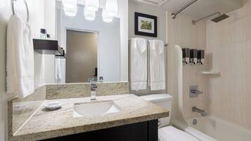 A bathroom with a granite countertop sink, a mirror, a toilet, a shower, and a towel rack.