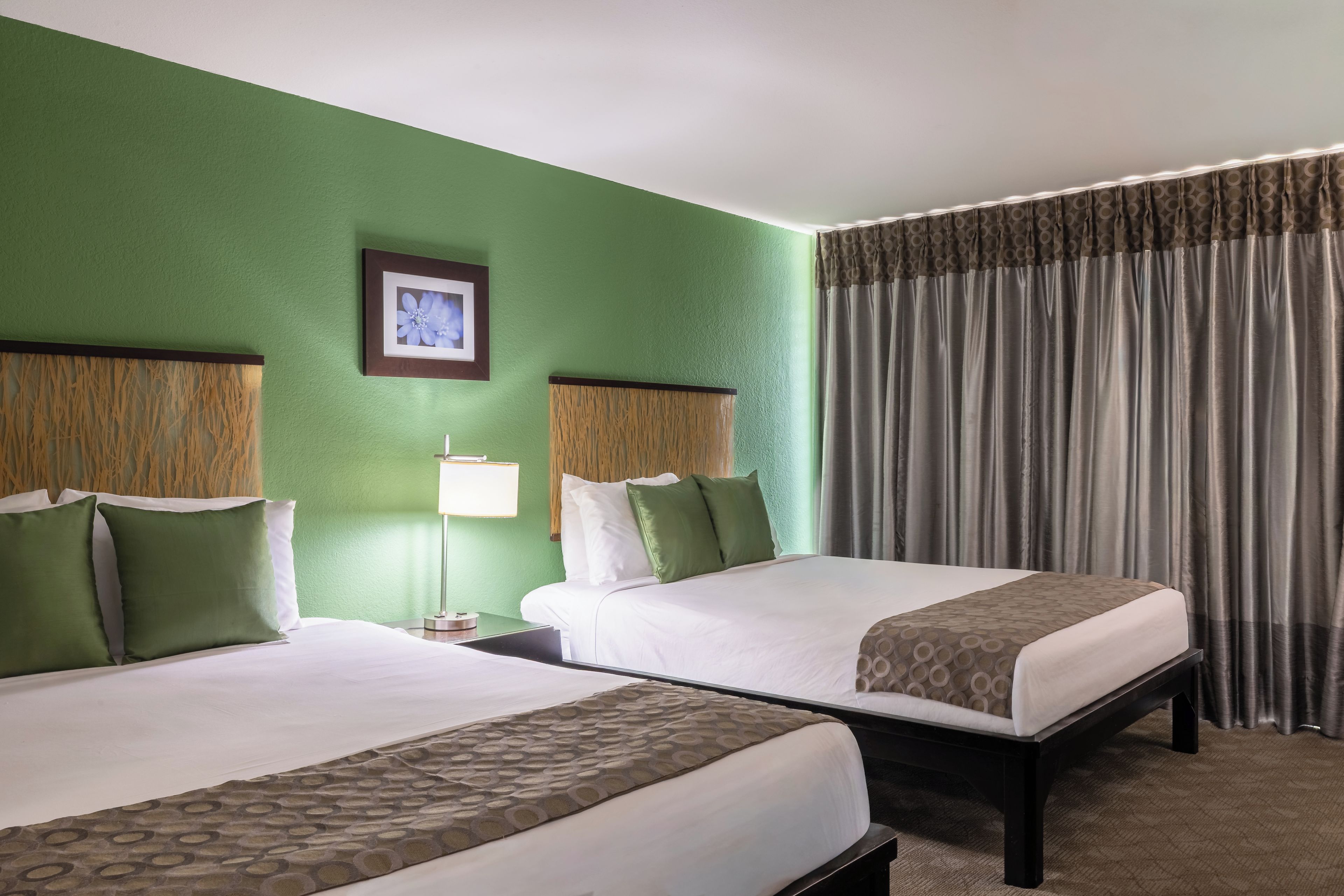 A hotel room with two beds, a green wall, a framed picture, and a window with curtains.
