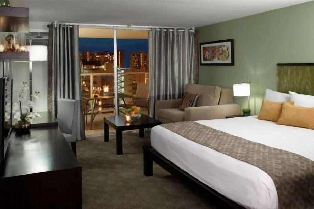 A hotel room with a bed, a sofa, a desk, and a view of the city at night.