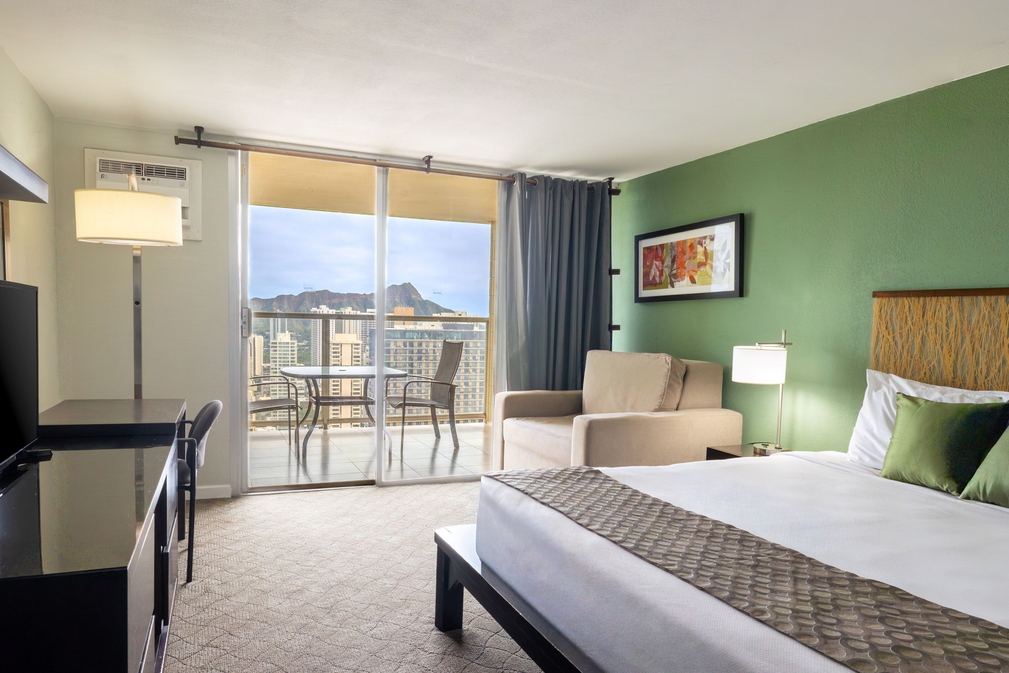 Een hotelkamer met een bed, een bureau, een stoel, een bank, een tafel en uitzicht op de stad.
