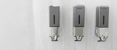 Three wall-mounted dispensers labeled 'shampoo,' 'shampoo,' and 'hair conditioner' in a bathroom with white tiled walls.