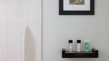 A bathroom with a shower, a framed picture on the wall, and a shelf with three toiletry bottles.