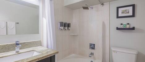 A bathroom with a bathtub, a toilet, a sink with a mirror, and a shower area.