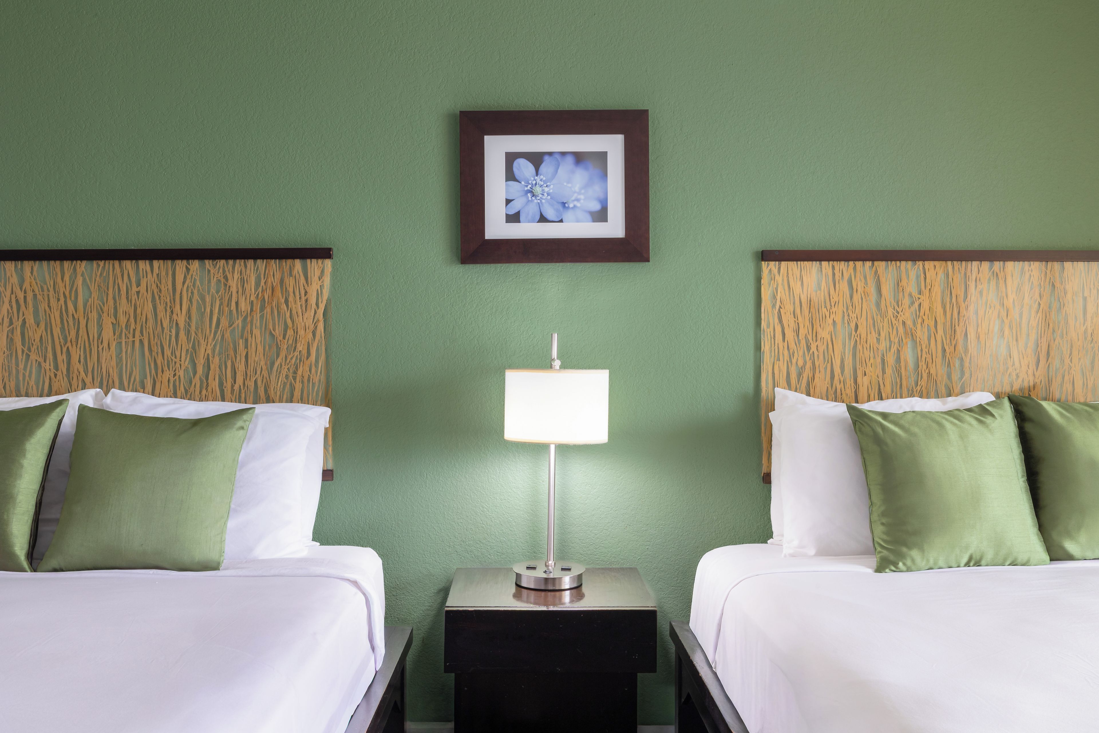 A hotel room with two beds, a nightstand with a lamp, and a framed picture on the wall.