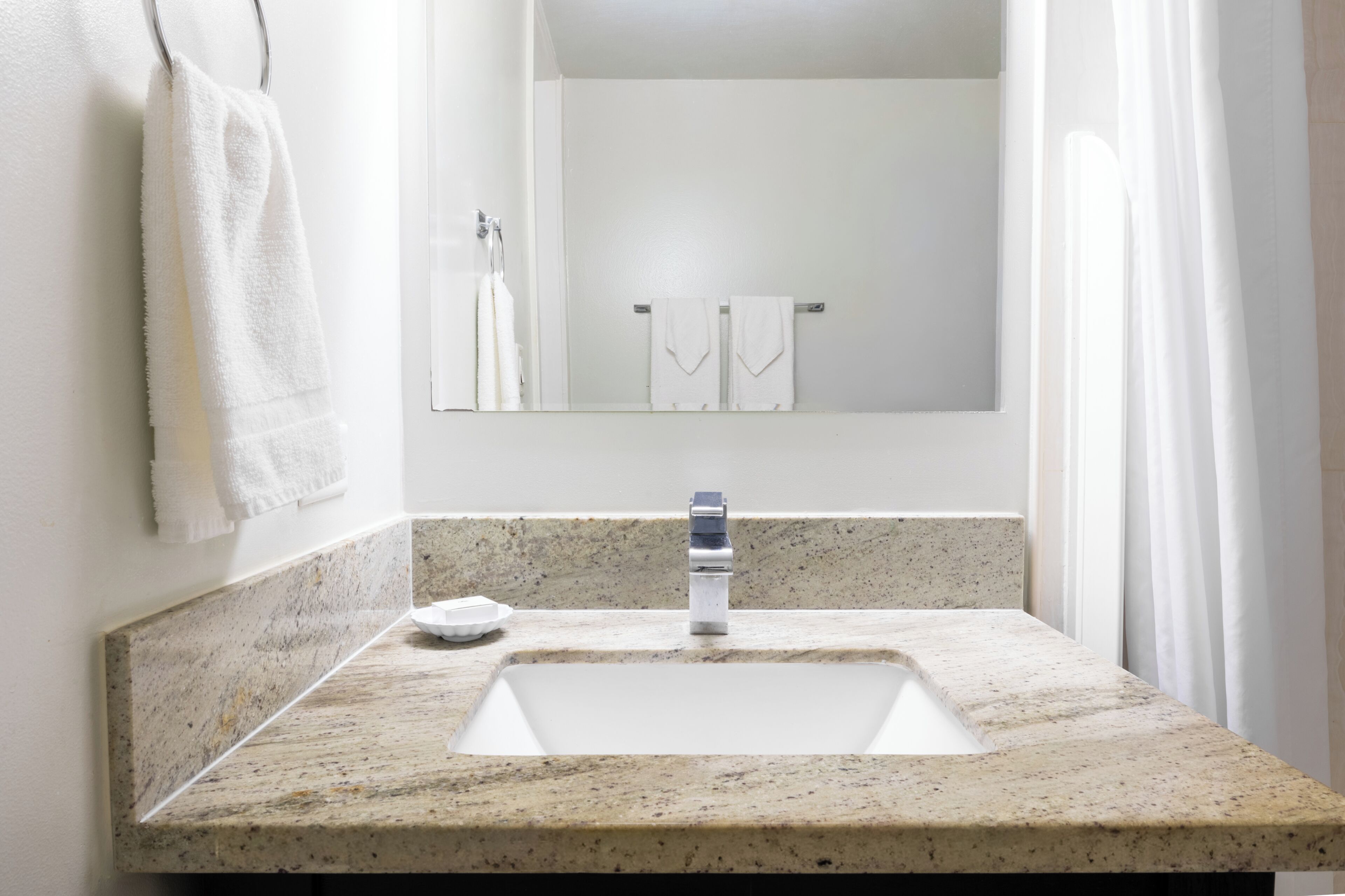 A bathroom with a granite countertop, a white sink, a mirror, and a towel rack.