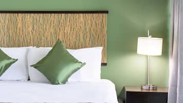 A neatly made bed with green and white pillows, a patterned bedspread, and a bedside lamp on a nightstand.