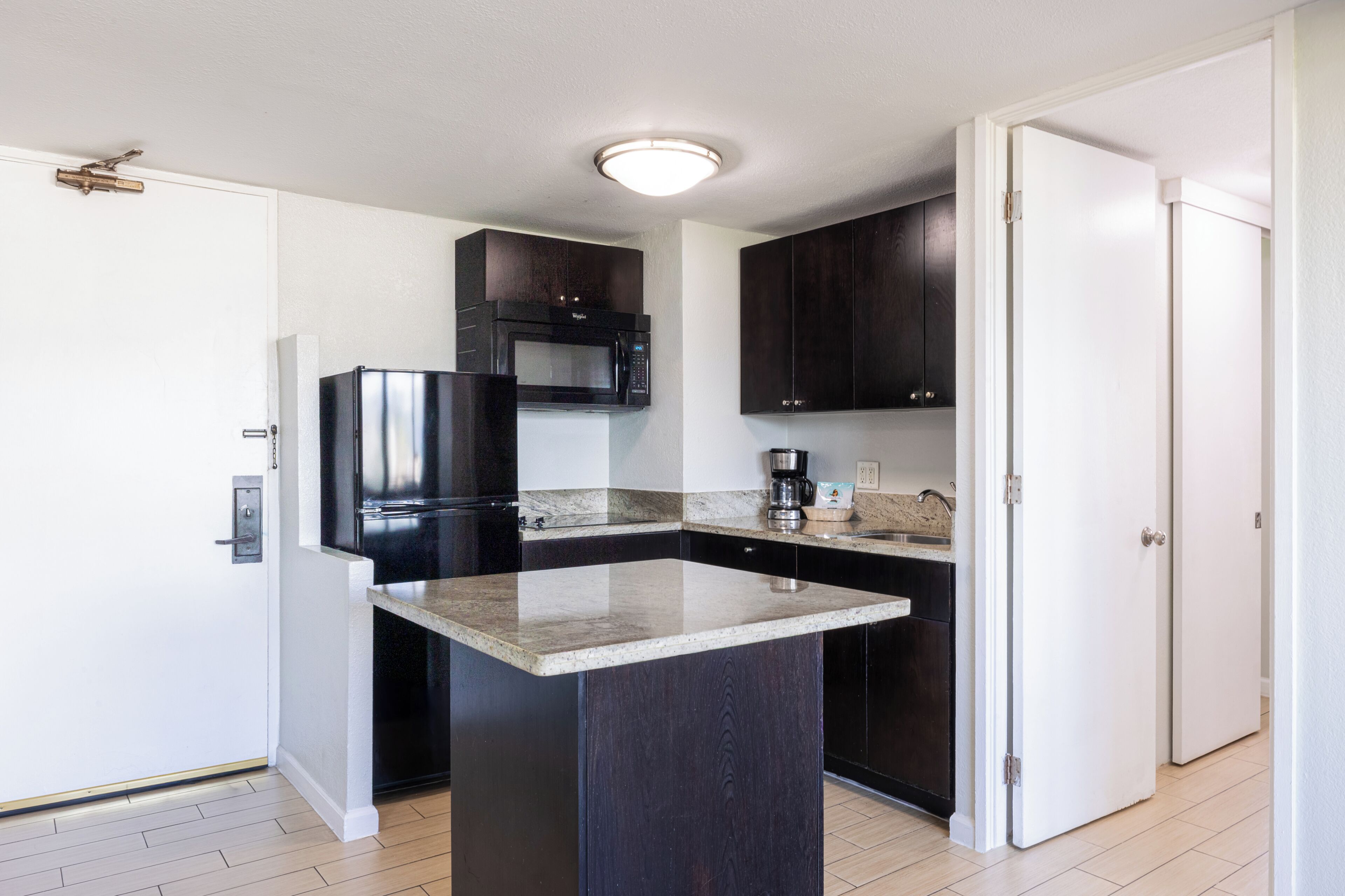 A kitchen with dark cabinets, a stainless steel refrigerator, a microwave, and a coffee maker.