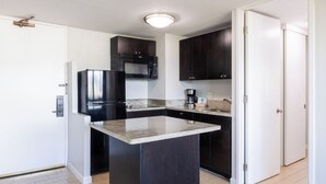 A kitchen with dark cabinets, a stainless steel refrigerator, a microwave, and a coffee maker. - Skyline Island Colony Hotel (Honolulu)