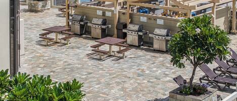 An outdoor patio with barbecue grills, picnic tables, and lounge chairs.