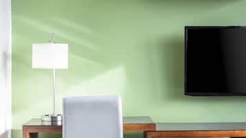 Una habitación con pared verde, televisor de pantalla plana, escritorio con lámpara, una silla y un armario de madera.