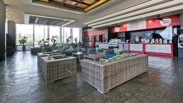 A spacious lobby with wicker furniture, a Pepsi sign, and a large window offering a view of greenery.