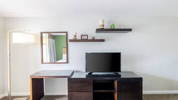 Une chambre moderne avec un téléviseur à écran plat posé sur un bureau en bois foncé, un lampadaire et un miroir accroché au mur.