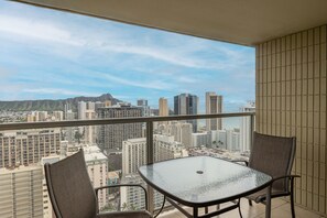 A balcony with a table and chairs, overlooking a cityscape with high-rise buildings and mountains. - Skyline Island Colony Hotel (Honolulu)