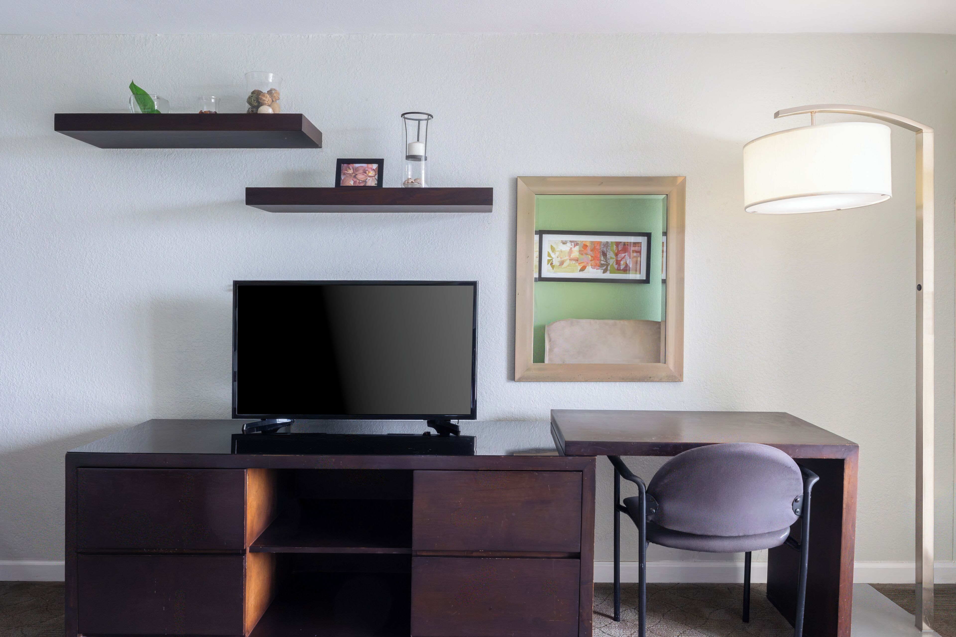 A modern room with a flat-screen TV, dark wooden desk, chair, and shelves with decorative items.