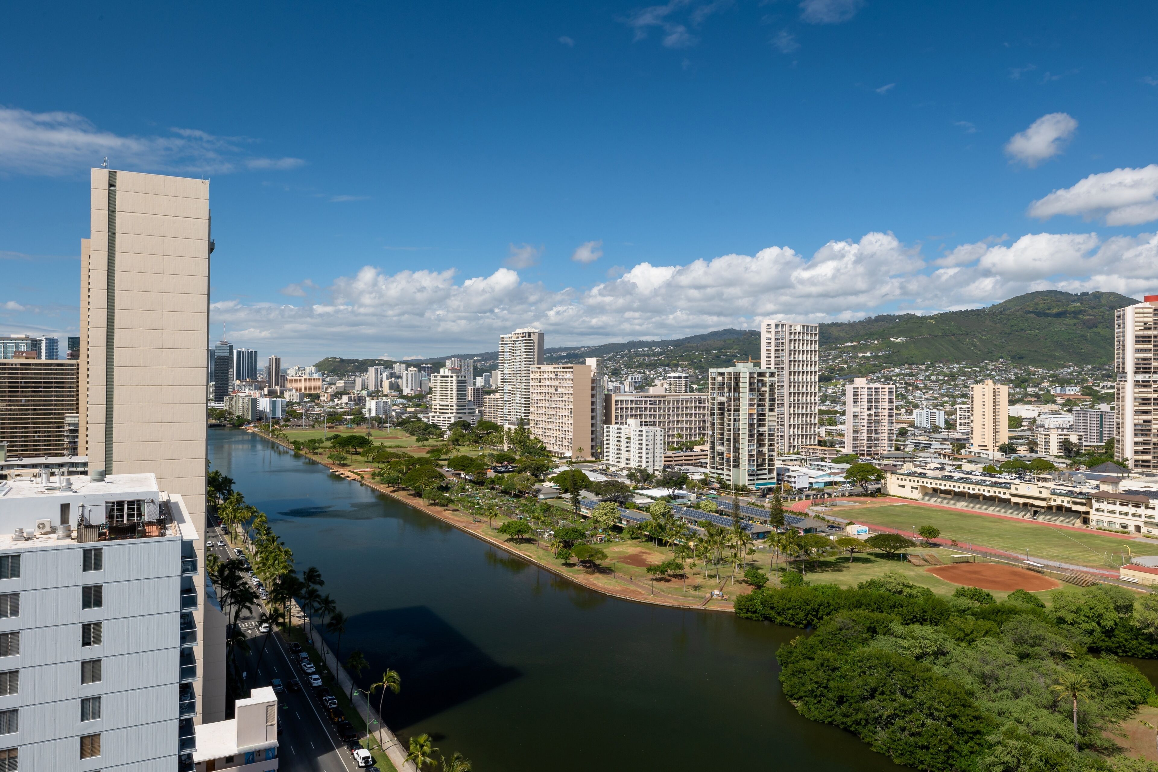 A cityscape with a river, high-rise buildings, and a park with a sports field.