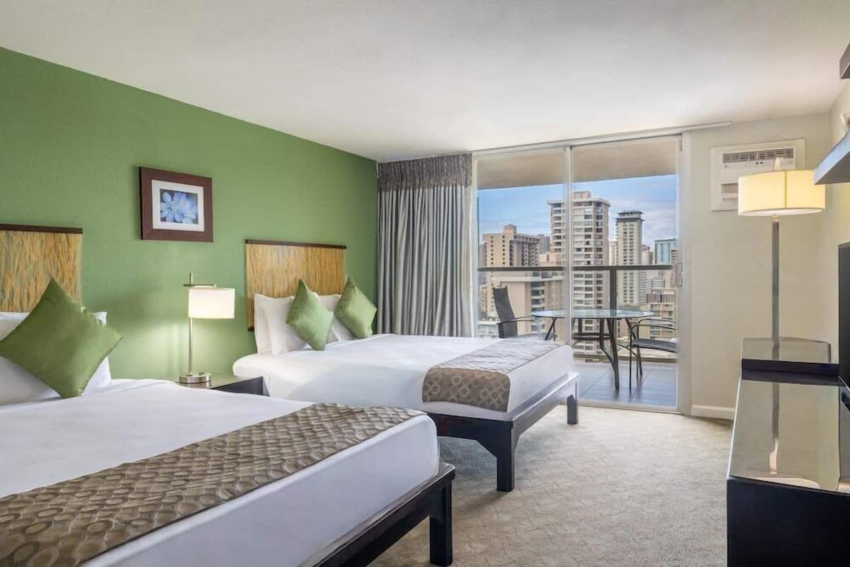 A hotel room with two beds, a balcony with a city view, a desk, and a chair.